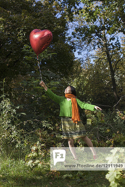Volle Länge einer fröhlichen Frau mit rotem Herzballon im Park