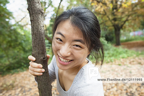 Portrait of smiling woman holding tree trunk while standing at park