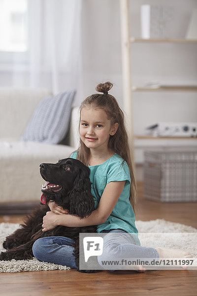Portrait of cute girl embracing dog while sitting on rug at home