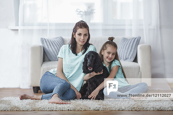 Porträt von Mutter und Tochter mit Hund  der zu Hause auf einem Teppich sitzt.
