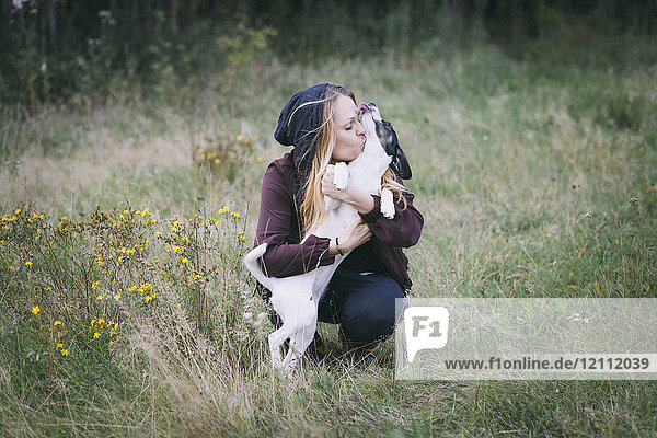 Frau küsst Hund beim Hocken im Grasfeld