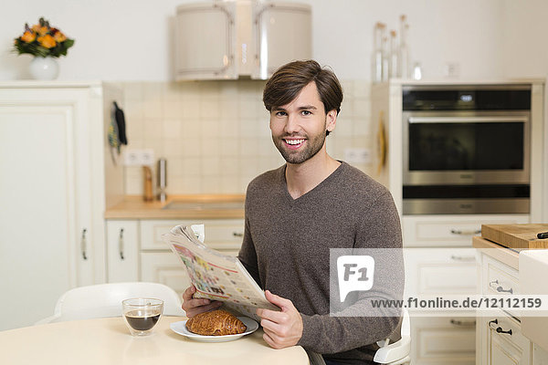 Porträt eines lächelnden Mannes am Frühstückstisch mit Zeitung