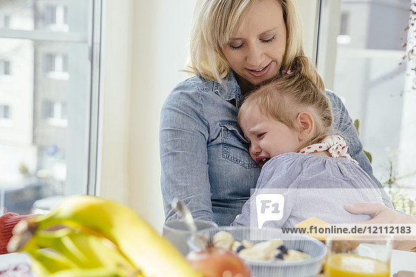 Kleines Mädchen weint in den Armen der Mutter am Frühstückstisch