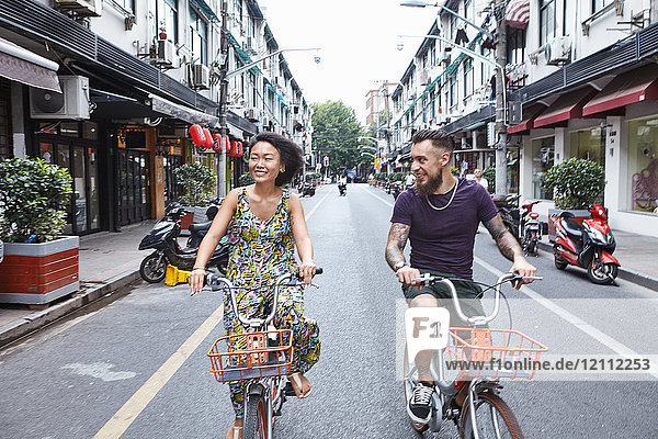 Multi-ethnisches Hipster-Paar radelt entlang der Stadtstraße  Shanghai Französische Konzession  Shanghai  China