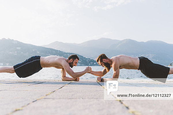 Two young men doing push ups on waterfront  Lake Como  Lombardy  Italy