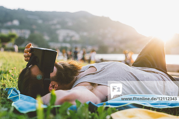 Young male hipster lying on grass looking at virtual reality headset  Lake Como  Lombardy  Italy