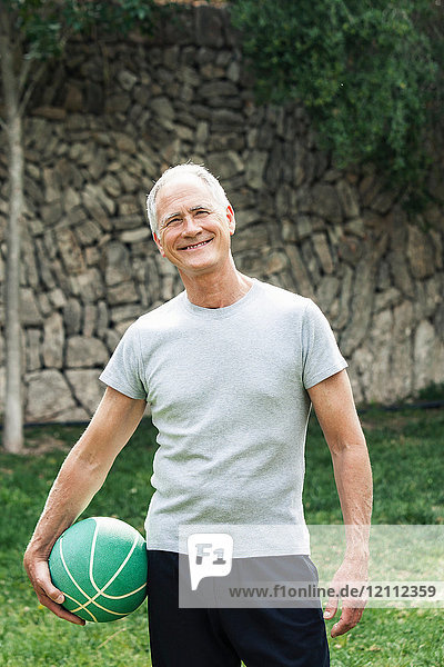 Porträt eines Mannes  der einen Basketball hält und lächelnd in die Kamera schaut
