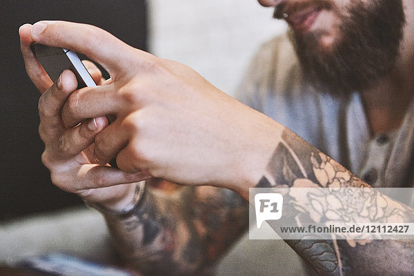 Hände eines tätowierten jungen männlichen Hipsters  der ein Smartphone hält  Nahaufnahme