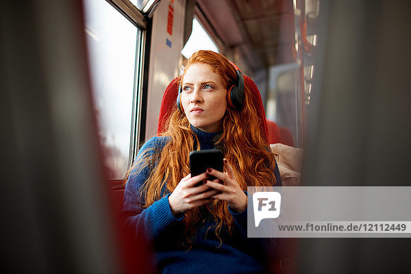 Frau im Zug  die mit Kopfhörern Musik auf Mobiltelefonen hört  London