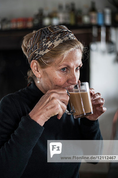 Blonde ältere Frau mit blonden Haaren trinkt Kaffee in der Küche