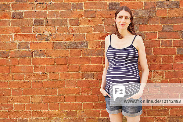 Porträt einer schwangeren Frau im mittleren Erwachsenenalter an einer Ziegelmauer