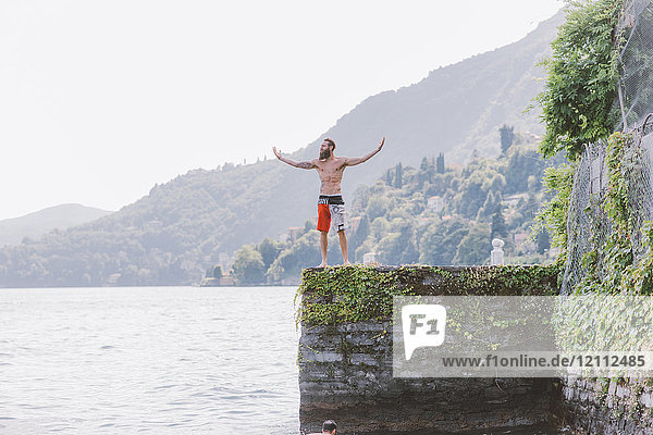 Junger männlicher Schwimmer steht mit offenen Armen am Pier  Comer See  Lombardei  Italien