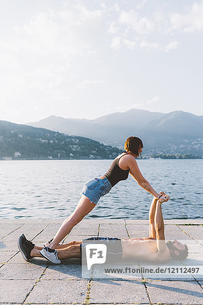 Junge Frau balanciert mit ihrem am Wasser liegenden Freund  Comer See  Lombardei  Italien