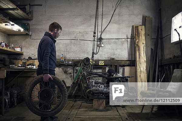 Mechanic carrying vintage motorcycle wheel in workshop