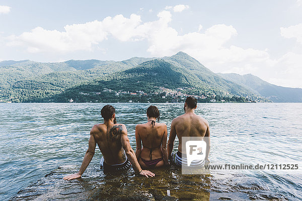 Rückansicht von drei jungen erwachsenen Freunden  die am Comer See sitzen  Como  Lombardei  Italien