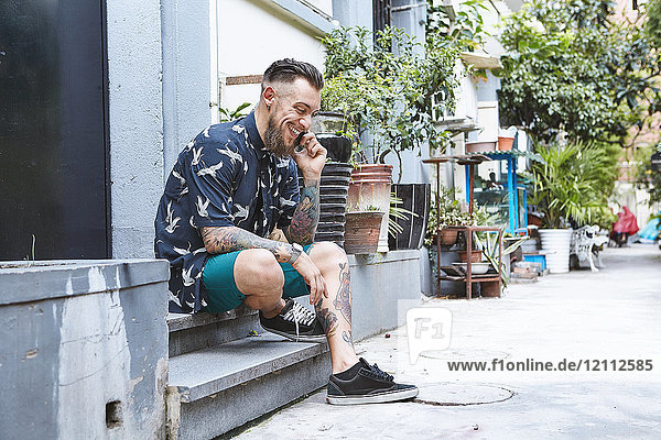 Junger Mann sitzt auf der Türschwelle in einer Wohngasse und telefoniert mit einem Smartphone  Shanghai Französische Konzession  Shanghai  China