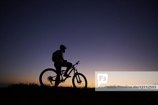 Silhouettierter männlicher Mountainbiker mit Blick auf den Sonnenuntergang