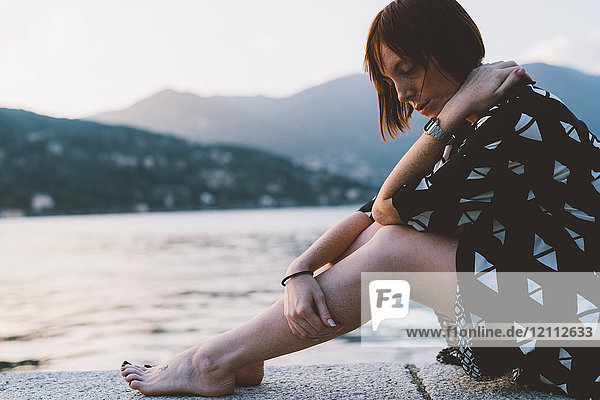Young woman sitting on waterfront wall by Lake Como  Lombardy  Italy