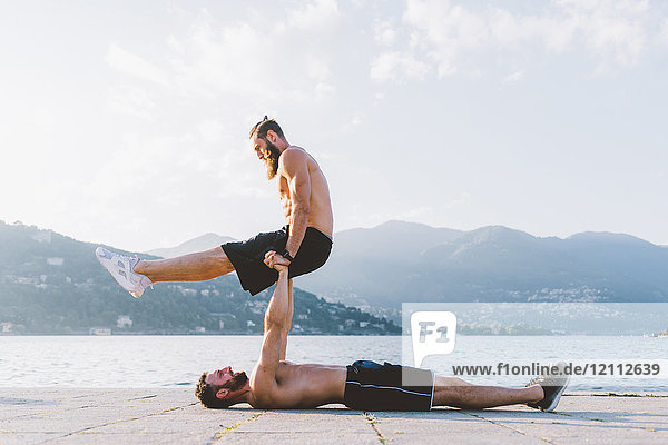 Young man lying on back supporting friend on waterfront  Lake Como  Lombardy  Italy