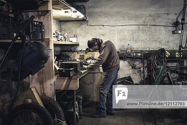 Mechanic working at bench with dismantled vintage motorcycle in workshop