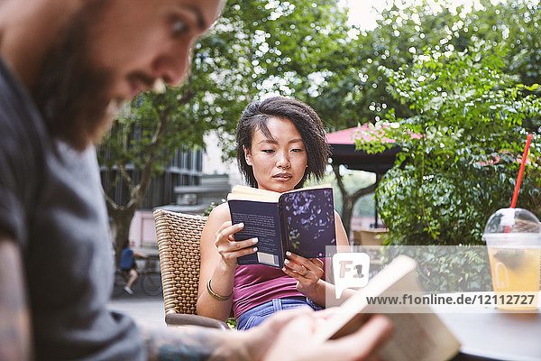 Multi ethnic hipster couple reading books at sidewalk cafe  Shanghai French Concession  Shanghai  China