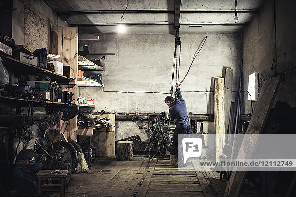 Mechanic hoisting dismantled vintage motorcycle in workshop