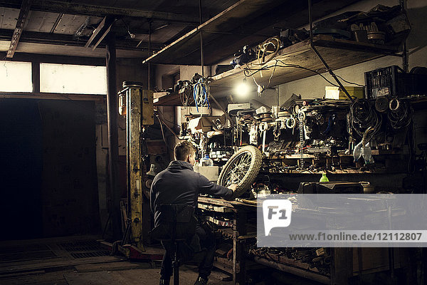 Mechanic repairing vintage motorcycle wheel at workshop bench