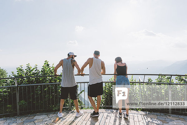 Rückansicht von drei jungen erwachsenen Freunden  die vom Balkon auf den Comer See blicken  Como  Lombardei  Italien