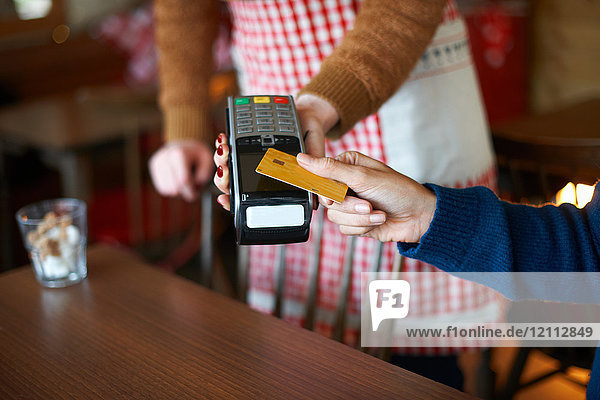 Kunde im Café  der kontaktlos mit Kreditkarte bezahlt