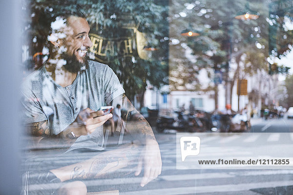 Junger männlicher Hipster im Cafe-Fenstersitz mit Smartphone in der Hand  Shanghai Französische Konzession  Shanghai  China