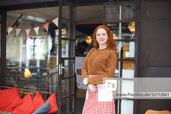 Portrait of small business owner in front of cafe looking at camera smiling