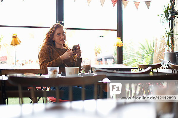 Frau mit Smartphone entspannt sich im Cafe