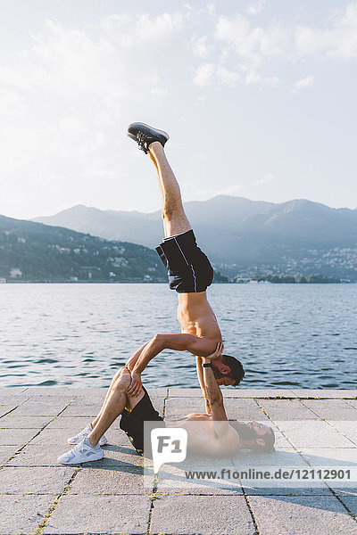 Two young men doing team handstand on waterfront  Lake Como  Lombardy  Italy
