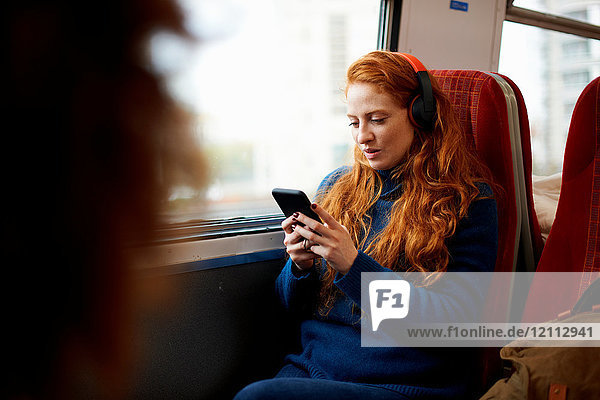 Woman on train listening to music on mobile phone with headphones  London