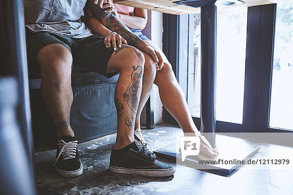 Taille eines multiethnischen Hipster-Paares im Café mit der Hand auf dem Knie des anderen  Schanghai Französische Konzession  Schanghai  China