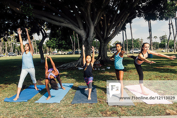 Girls and teenage schoolgirls practicing yoga warrior pose on school playing field