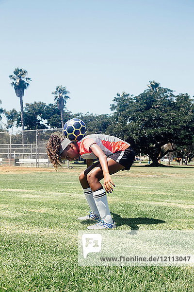 Teenager-Schülerin Fussballspielerin balanciert Ball auf Schultern auf dem Schulsportplatz