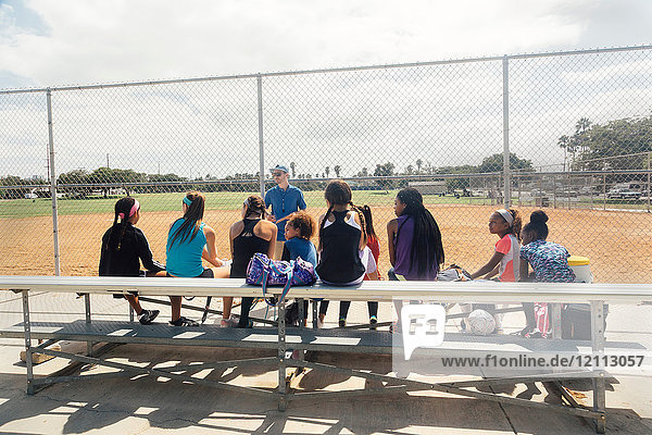 Männlicher Lehrer unterweist Schulmädchen-Fussballspieler auf der Sportplatzbank der Schule