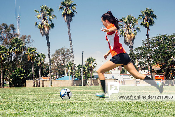 Teenager-Schülerin rennt  um einen Fussball auf dem Schulsportplatz zu kicken