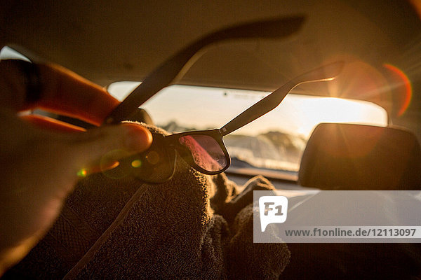 Junger Mann wischt Sonnenbrille im sonnenbeschienenen Auto  Nahaufnahme
