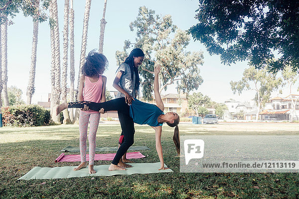 Mädchen und jugendliche Schülerinnen  die Yoga praktizieren  stellen sich im Halbmond stehend auf dem Schulhof in Halbmondpose