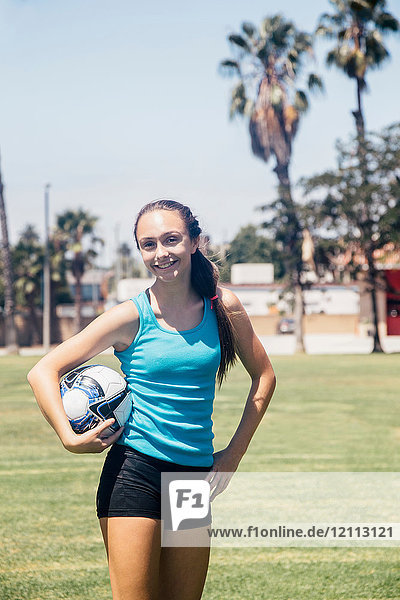 Portrait of schoolgirl soccer player holding soccer ball on school sports field