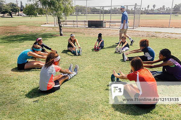 Lehrer unterrichtet Schulmädchen-Fussballspielerinnen beim Aufwärmen auf dem Schulsportplatz