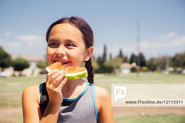 Schulmädchen isst Melonenscheibe auf Schulsportplatz