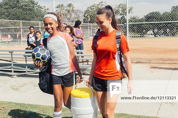 Schulmädchen tragen Kühlbox zum Fußballtraining auf dem Schulsportplatz