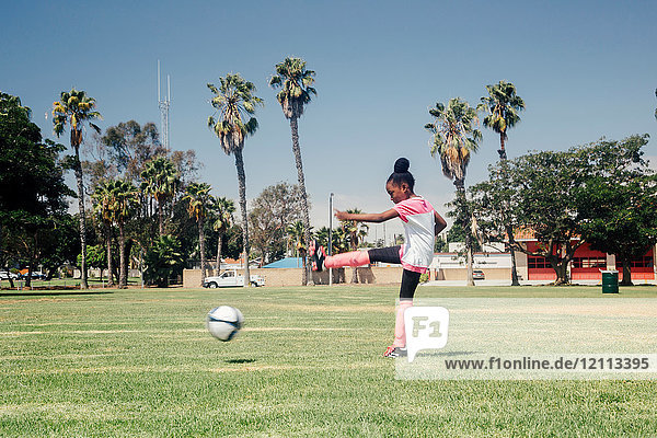 Schoolgirl kicking soccer ball on school sports field