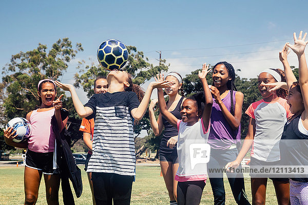Schoolgirl soccer team watching player balancing soccer ball on nose on school sports field