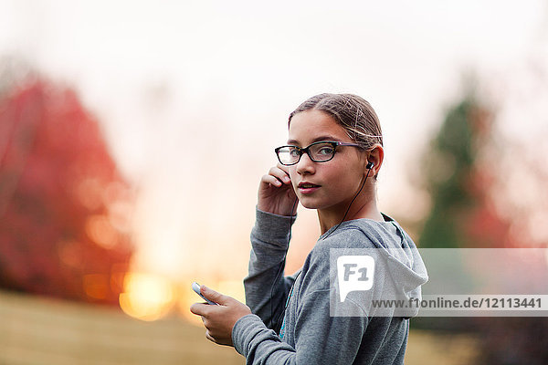 Portrait of girl listening to smartphone earphone music looking over her shoulder in garden
