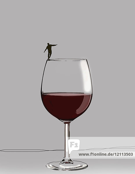 Man balancing precariously on rim of large wine glass