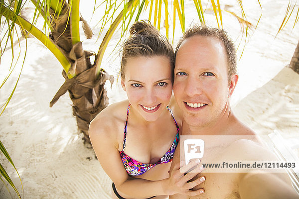 Young couple taking a self-portrait on a tropical beach; Negril Jamaica